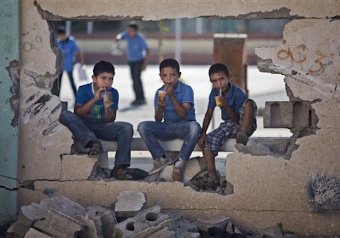 Palestinian school boys drink iced juice as they sit on a damaged wall of a school in Gaza City