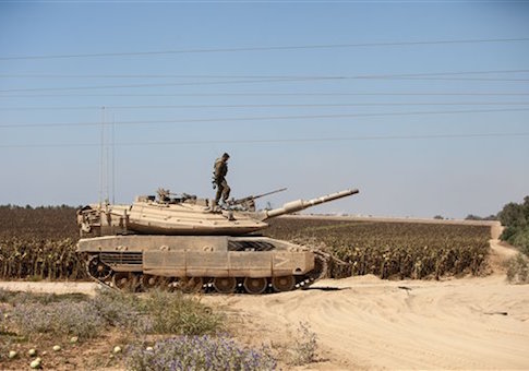 An Israeli soldier is standing on the top of a tank, near the border with Gaza