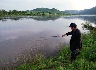 Chinese farmer fishes across from farmland in North Korea